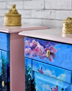 Detaliu pictură manuală pe noptieră roz – nori roz, cer albastru și fluturi, mobilier artistic recondiționat