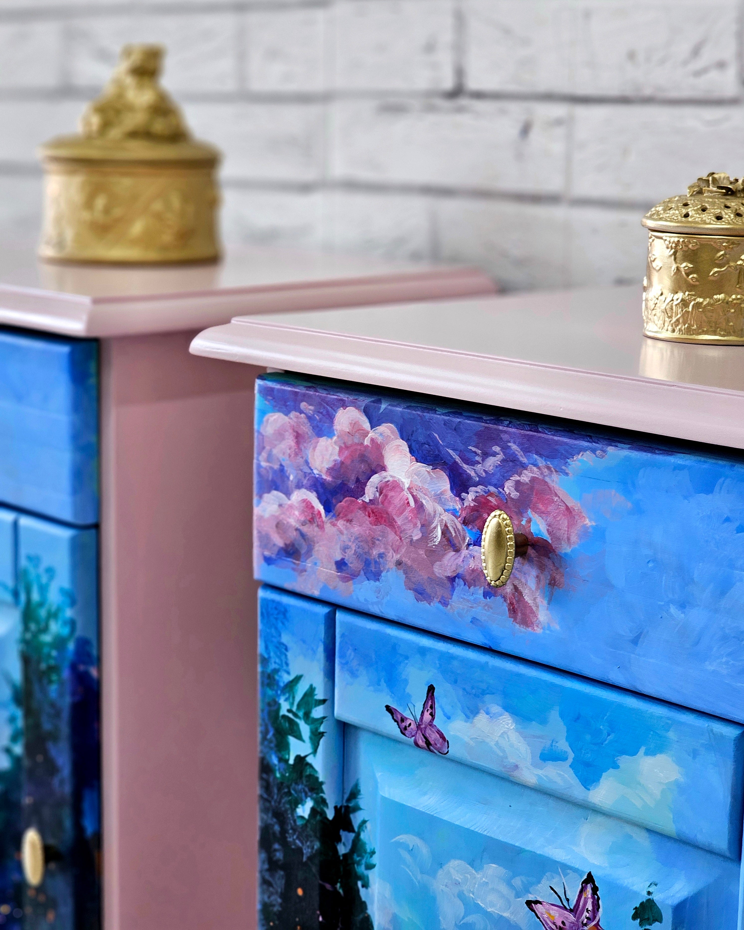 Detaliu pictură manuală pe noptieră roz – nori roz, cer albastru și fluturi, mobilier artistic recondiționat