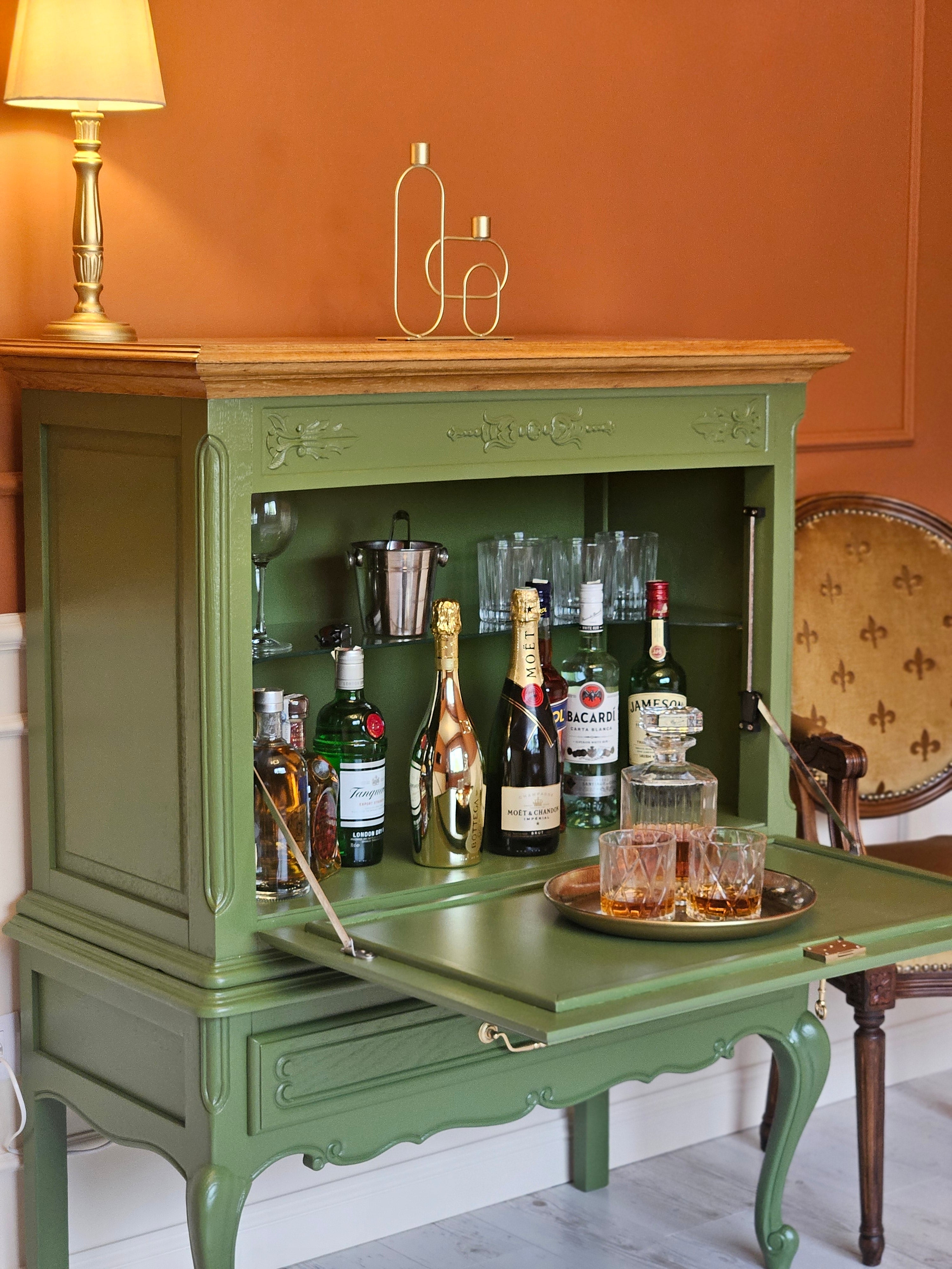 Gros-plan lateral al unui minibar verde elegant, cu sticle de vin și pahare.